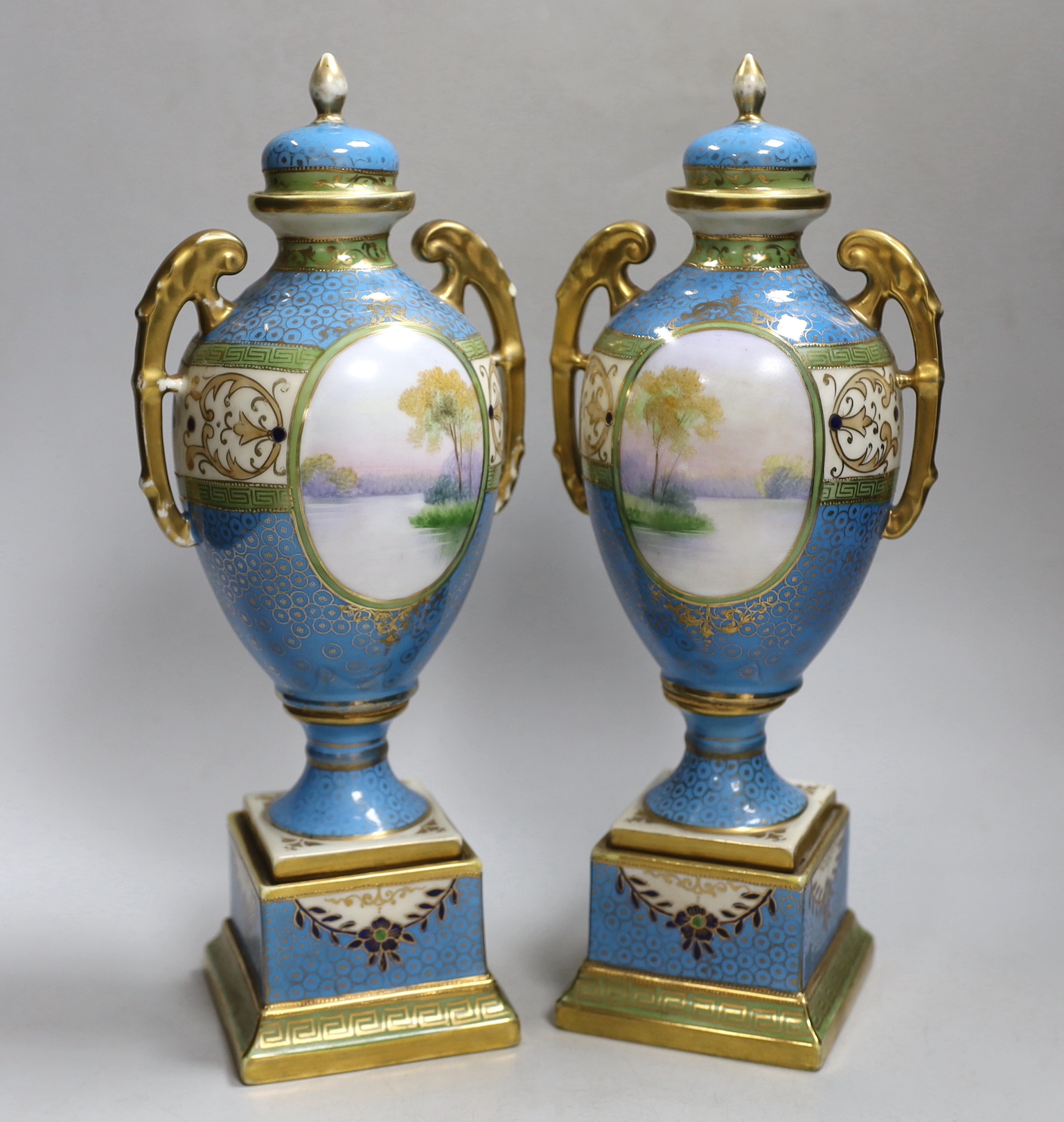 A pair of Japanese Noritake vases and covers, each hand painted with a river landscape, 29cm high